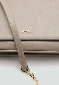 Borsa in finta pelle beige con una texture liscia, un logo dorato "MNG" e una tracolla a catena removibile con maglie rotonde.