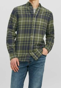 Grün-blau kariertes Hemd zum Zumachen aus weichem Stoff, mit langen Ärmeln und einer Brusttasche; getragen mit Jeans.