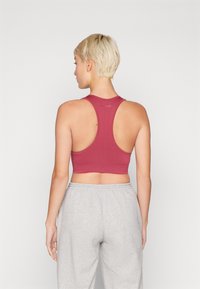 Top desportivo vermelho, cortado, com um design de costas nadador. Tecido suave e faixa elástica proporcionam conforto. Combinado com calças de moletão cinzas.