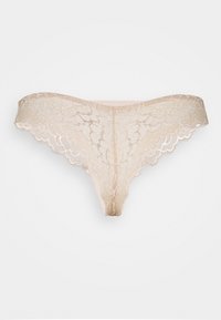 Spetsstring i nude-färg med vågiga kanter och blommönster. Mjukt tyg med en slät textur och minimal baksidestäckning.