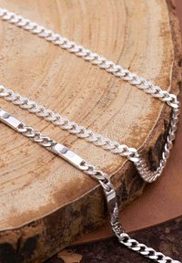 Bijoux en chaîne argentée posés sur une surface en bois. Comprend des maillons entrelacés, une finition lisse et des largeurs de maillon variées.