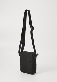 Sac bandoulière noir en tissu texturé, avec une sangle ajustable et une fermeture éclair, au design carré compact.