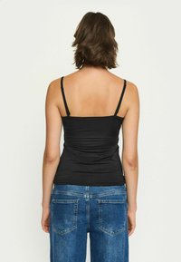 Čierna priliehavá tielko s tenkými nastaviteľnými ramienkami, s naťahovanými detailami na chrbte, spárované so stredne vysokými modrými džínsami.