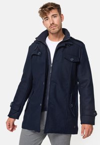 Navy wool blend coat with a zip and button closure, side pockets, epaulets, and a stand collar. Features a textured finish.