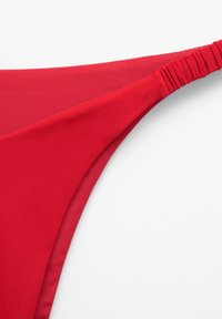 Pantalonii scurți de bikini roșii, cu o textură netedă, prezentând un brâu strâns și un design minimalist. Materialul are o calitate moale și elastică.