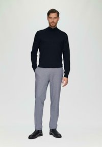 Marinefarbener Rollkragenpullover, graue gemusterte Hose, schwarze Stiefeletten; glatte Textur, figurbetonter Schnitt, lässiges Design. Minimalistischer Hintergrund.