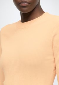 Broskyňový rebrovaný pletený sveter s okrúhlym výstrihom a dlhými rukávmi, s mäkkou textúrou a priliehavým strihom.