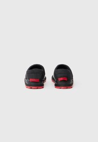 Zapatos negros tipo slip-on con textura acolchada, acentos rojos y una suela con diseño; presenta la marca "REPLAY" en el talón.