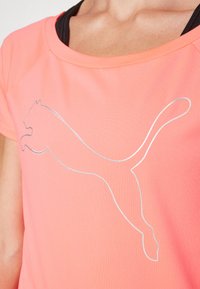 Rózsaszín sportpóló, rövid ujjú, az elején egy ezüst keretes ugró pumát ábrázoló logóval. Sima szövet textúra.