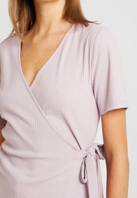 Vestido de color púrpura claro con canalé, escote en V, mangas cortas y diseño envolvente, con un detalle de lazo en el costado para un ajuste ajustable.