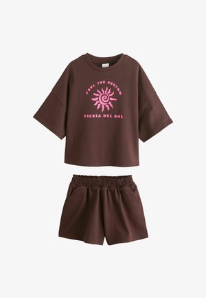 Pruun lühikeste varrukatega top roosa päikese graafika ja tekstiga „Feel the Rhythm Fiesta del Sol”, sobitatud pruuni elastse vöökohaga lühikeste pükstega.