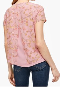Blusa a maniche corte rosa con motivo floreale, pannello posteriore trasparente e orlo arrotondato. Tessuto morbido, materiale leggero, abbinata a jeans scuri.