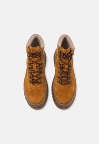 Botas de senderismo de ante marrón con una superficie texturizada, un collar acolchado y cordones en naranja y negro en contraste. Suela de goma gruesa para mayor tracción.