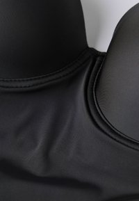 Černá polstrovaná podprsenka s hladkým materiálem, disponující bezešvou konstrukcí a zakřivenými košíčky. Šité detaily podél okrajů pro zesílení.