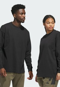 Sorte langærmede T-shirts lavet af blødt bomuldsstof, med rund hals og afslappet pasform. Begge har minimal branding, sat mod en lys baggrund.