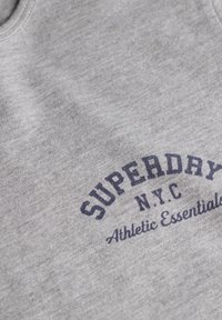Débardeur en coton gris avec un col rond et un logo imprimé en texte bleu foncé, indiquant "SUPERDRY NYC Athletic Essentials."
