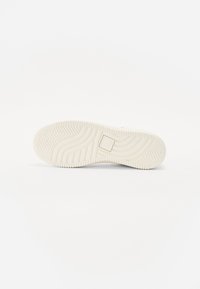 Sålen på en sneakers i lys cremefarve, med et tekstureret zigzag-mønster og et rektangulært logo-detalje. Blødt, gummiagtigt materiale.