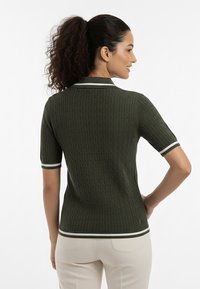 Zielona dzianinowa koszulka polo z krótkimi rękawami. Posiada teksturowany wzór warkocza oraz kontrastujące białe wykończenie na kołnierzyku i krawędziach rękawów.