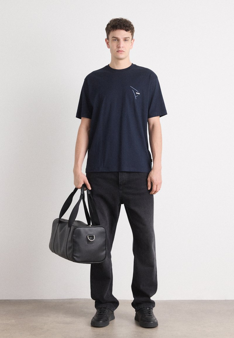 Camiseta de algodón azul marino con mangas cortas y un pequeño gráfico; combinada con pantalones de mezclilla negros y un bolso de piel negro.