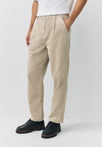 Beige corduroy trousers with side pockets, straight fit, and textured fabric, paired with black leather shoes featuring a thick sole.
