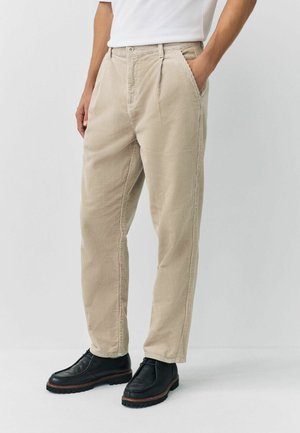 Beige corduroy trousers with side pockets, straight fit, and textured fabric, paired with black leather shoes featuring a thick sole.