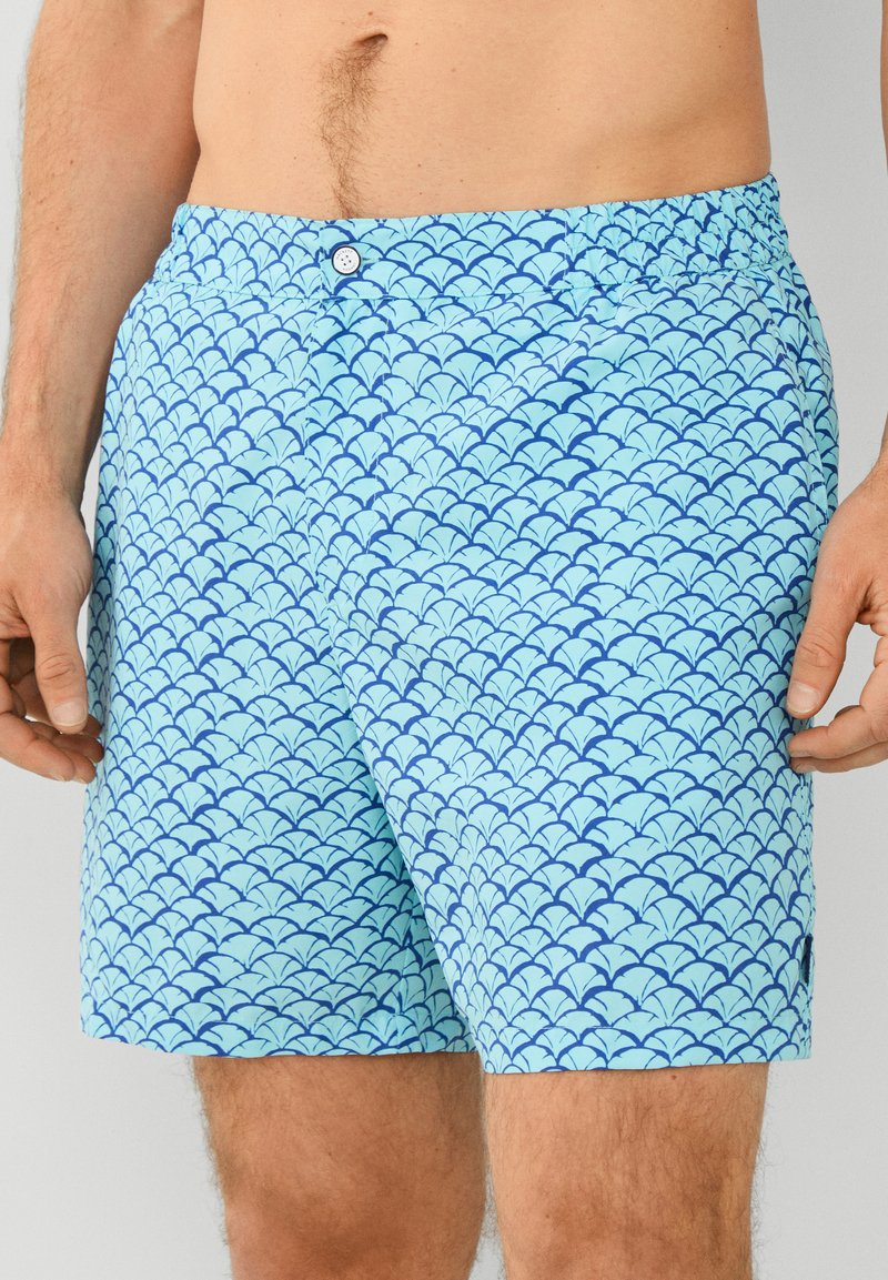 Plave kupaće gaće s uzorkom valova u tamnijoj plavoj boji. Pojas ima elastičan završetak s kopčanjem na dugme. Izrađene su od lagane tkanine.