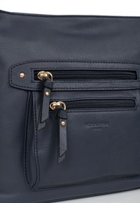 Borsa in pelle blu navy con hardware dorato, dotata di due tasche con zip e una texture liscia. Nome del brand impressa di lato.