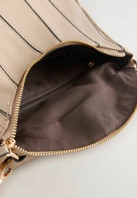 Interior de bolso de cuero beige con forro de tela marrón, con un compartimento con cremallera destacado por herrajes en tono dorado.