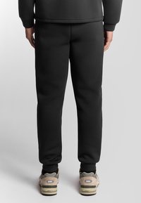 Zwarte sweatpants van zachte stof, met een taps toelopend ontwerp, een elastische tailleband en geribbelde manchetten. Gemaakt in combinatie met beige sneakers.