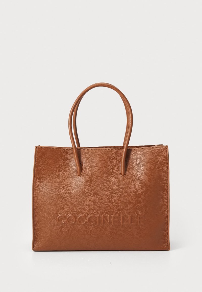 Sac fourre-tout en cuir tan avec deux poignées, présentant une surface texturée et un logo en relief à l'avant. Forme rectangulaire avec une fermeture éclair.