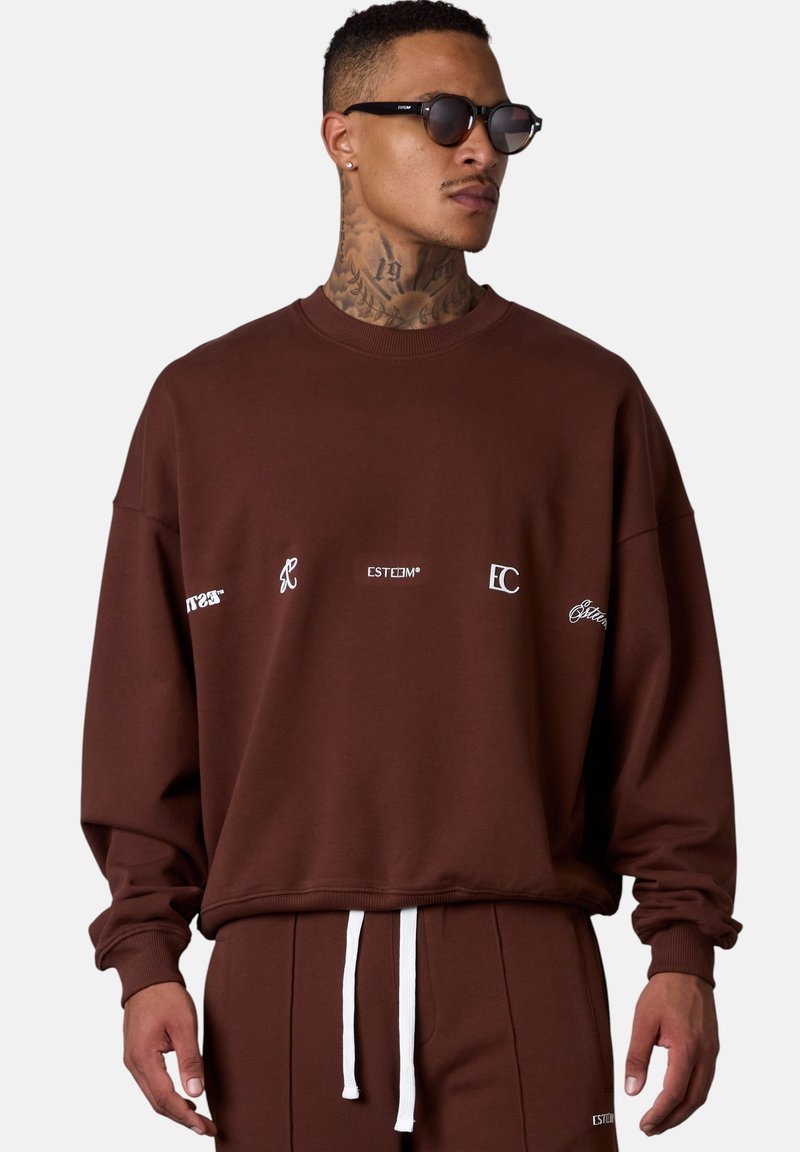 Brown sweatshirt with white logos, relaxed fit, crew neck, ribbed cuffs, and hem. Paired with matching pants featuring a white drawstring.