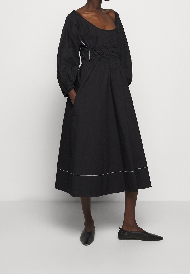 Svart midiklänning med fyrkantig halsringning, samlad midja, ballongärmar och en kontrasterande fållsöm. Kombinerad med svarta ballerina skor.