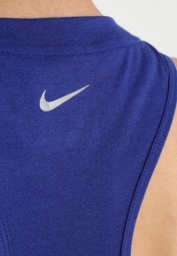 Gros plan sur l'épaule d'une personne portant un haut de sport bleu sans manches avec un logo blanc Nike swoosh dans le dos.