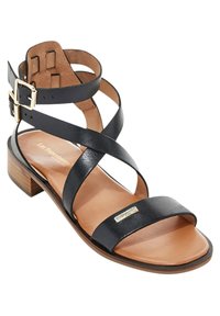 Sandalia de cuero negro con tiras entrelazadas y hebilla en el tobillo, con un tacón bajo de madera y una plantilla suave color bronceado. Acento con logo dorado presente.