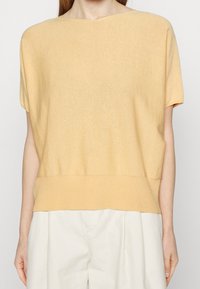 Żółty top z krótkim rękawem wykonany z miękkiego, lekkiego materiału o luźnym kroju, z prążkowanym dołem i minimalną liczbą szwów.