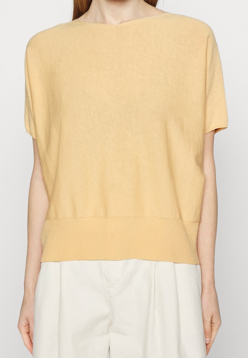 Żółty top z krótkim rękawem wykonany z miękkiego, lekkiego materiału o luźnym kroju, z prążkowanym dołem i minimalną liczbą szwów.