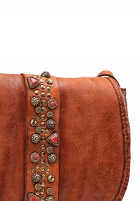 Borsa in pelle marrone con tracolla decorativa caratterizzata da borchie dorate e accenti di gemme rosse su sfondo bianco.