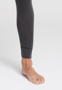 Mallas gris ajustadas hechas de material suave y elástico, que cuentan con un puño acanalado en el tobillo, combinadas con un pie descalzo.