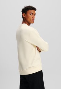 Cremefarvet sweatshirt lavet af bl�ødt stof, med rund hals, lange ærmer og et logo-accents på bagsiden af kanten.