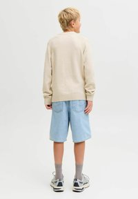 Bežinis fliso megztinis su raukšlėtais rankogaliais, derinamas su šviesiai mėlynomis džinsinėmis šortais. Modelis dėvi pilkas kojines ir margas sportines batus.