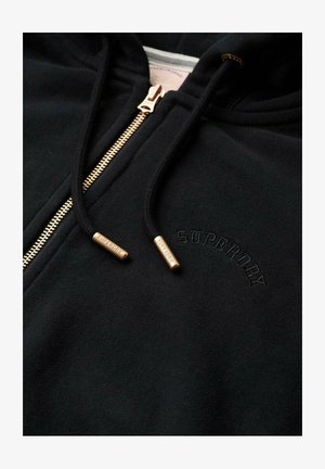 Zwarte hoodie met ritssluiting en gouden rits en metalen accenten, met een geborduurd "Superdry" logo in ton-sur-ton zwart op de borst. Zachte textuur.