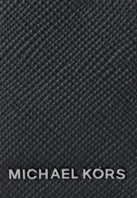 Sort tekstureret materiale med et krydsmønster; har et metallisk "MICHAEL KORS" logo i en blank finish nederst.