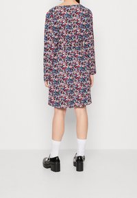 Blommönstrad, långärmad klänning i marinblått, rött och vitt; knälång design med en avslappnad passform och detalj vid ryggen. Svarta plattformsskor vidda.