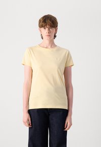 T-shirt di cotone gialla con maniche corte, scollatura rotonda e logo discreto dello stesso colore. Indossata con pantaloni in denim scuri.