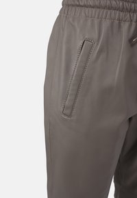 Hnedé kožené nohavice s hladkou textúrou, elastickým pásom a diskrétnou bočnou kapsou s prešitými okrajmi.