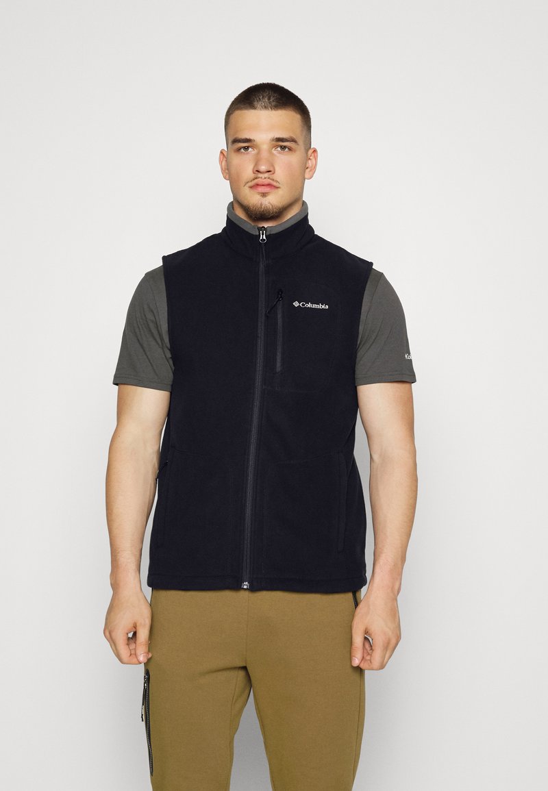 Schwarze Fleece-Weste mit Reißverschluss und hohem Kragen. Verfügt über zweiseitliche Taschen und eine Brusttasche, getragen über einem grauen kurzärmeligen Hemd.