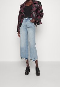 Läderjacka i svart och burgunder rutig design, i kombination med ljusblå vida jeans med fransar i kanten och svarta klackmules.