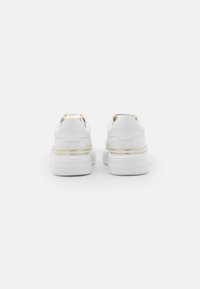 Sneakers bianchi con una finitura liscia, caratterizzati da una suola rialzata, un tallone con dettagli dorati e un design minimalista. La vista posteriore mostra texture a contrasto.