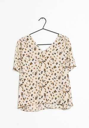 Blouse beige à manches courtes avec un col en V et un motif floral abstrait marron, noir et bleu marine, suspendue sur un cintre noir.