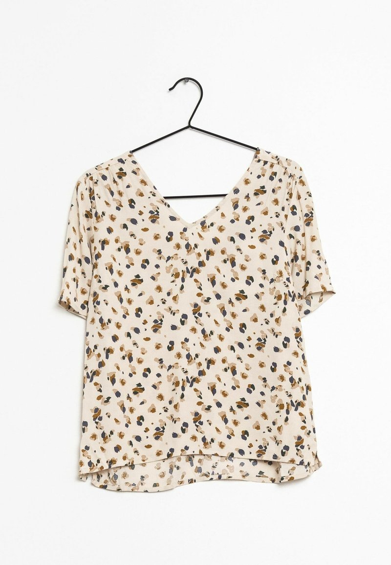 Blouse beige à manches courtes avec un col en V et un motif floral abstrait marron, noir et bleu marine, suspendue sur un cintre noir.